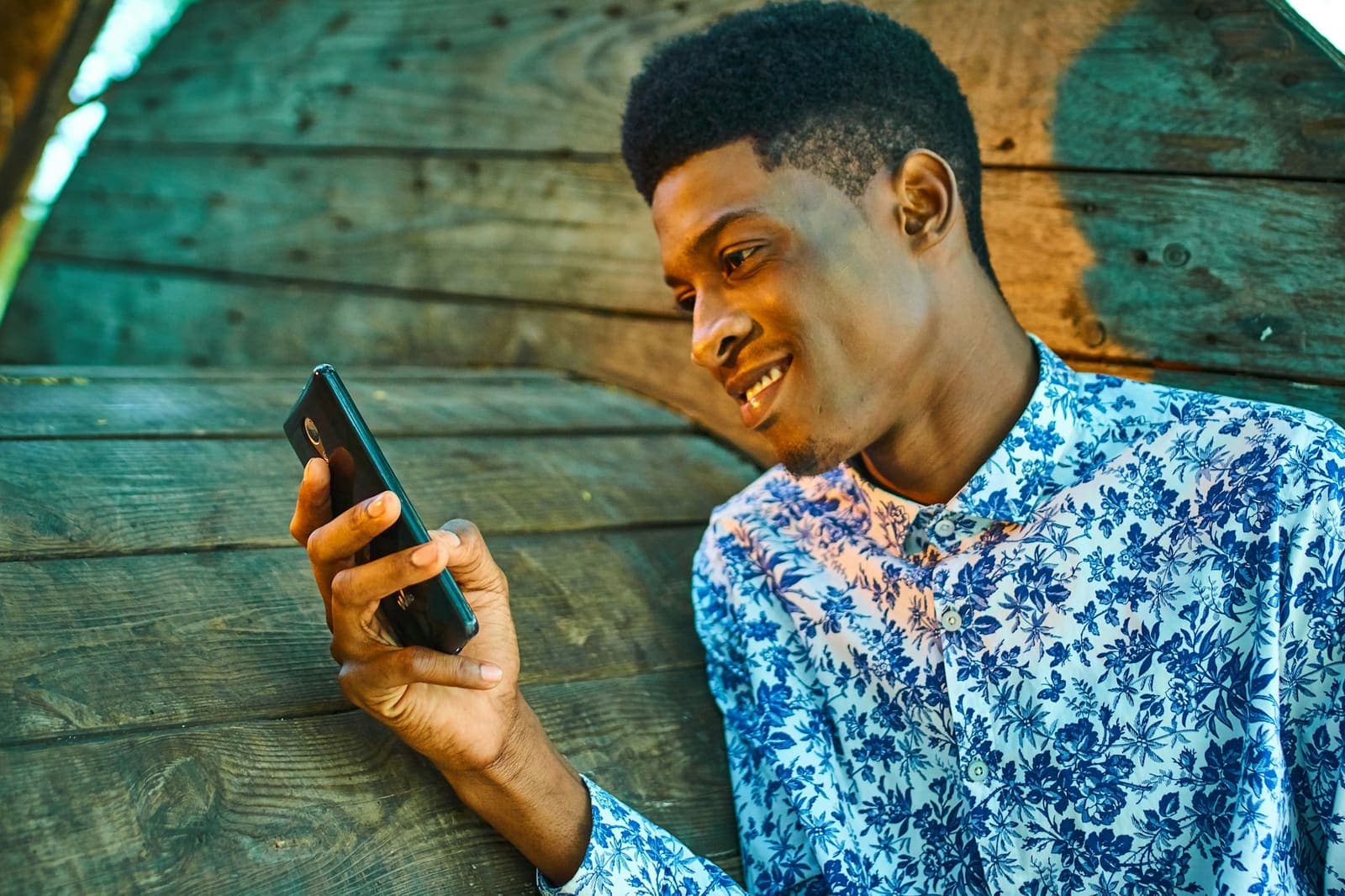 Un jeune homme sourit en écrivant sur son téléphone.